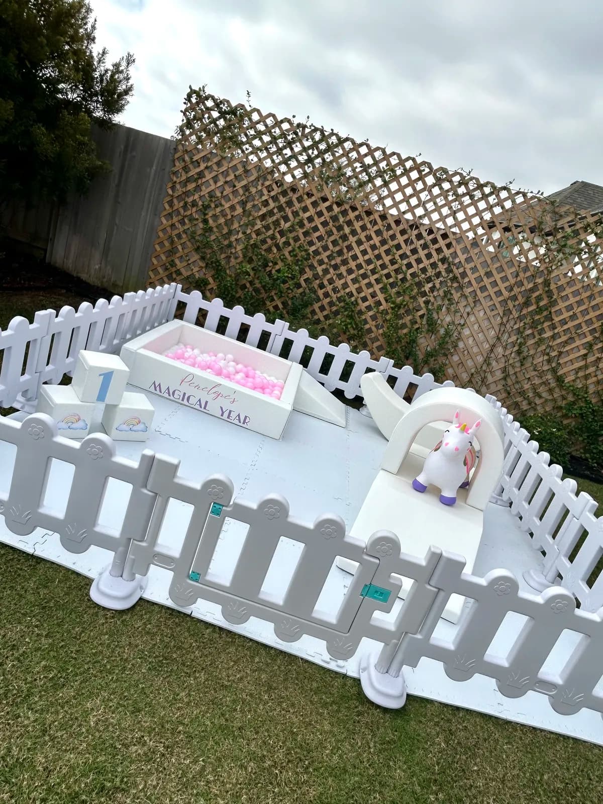 Garden party soft play setup on the lawn with a unicorn rocker and name sign