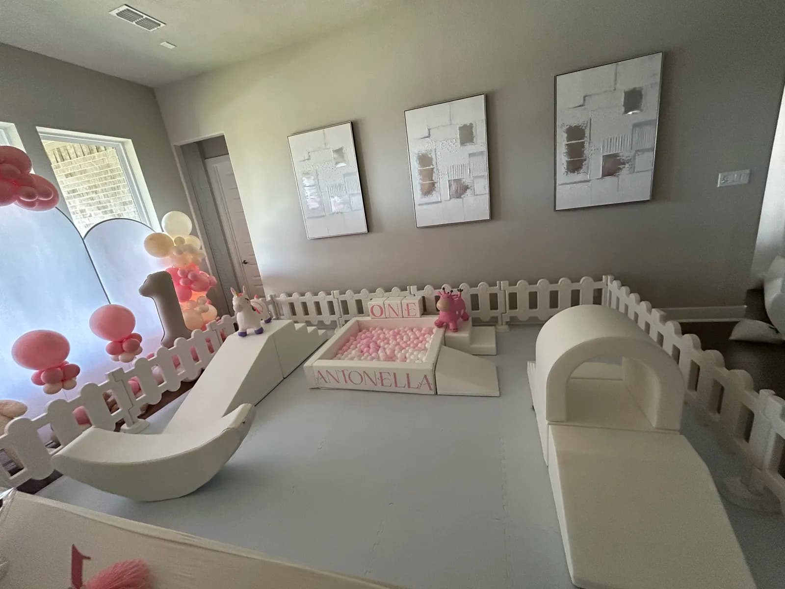 Birthday party setup with a pink balloon arch, slide, and personalized ball pit