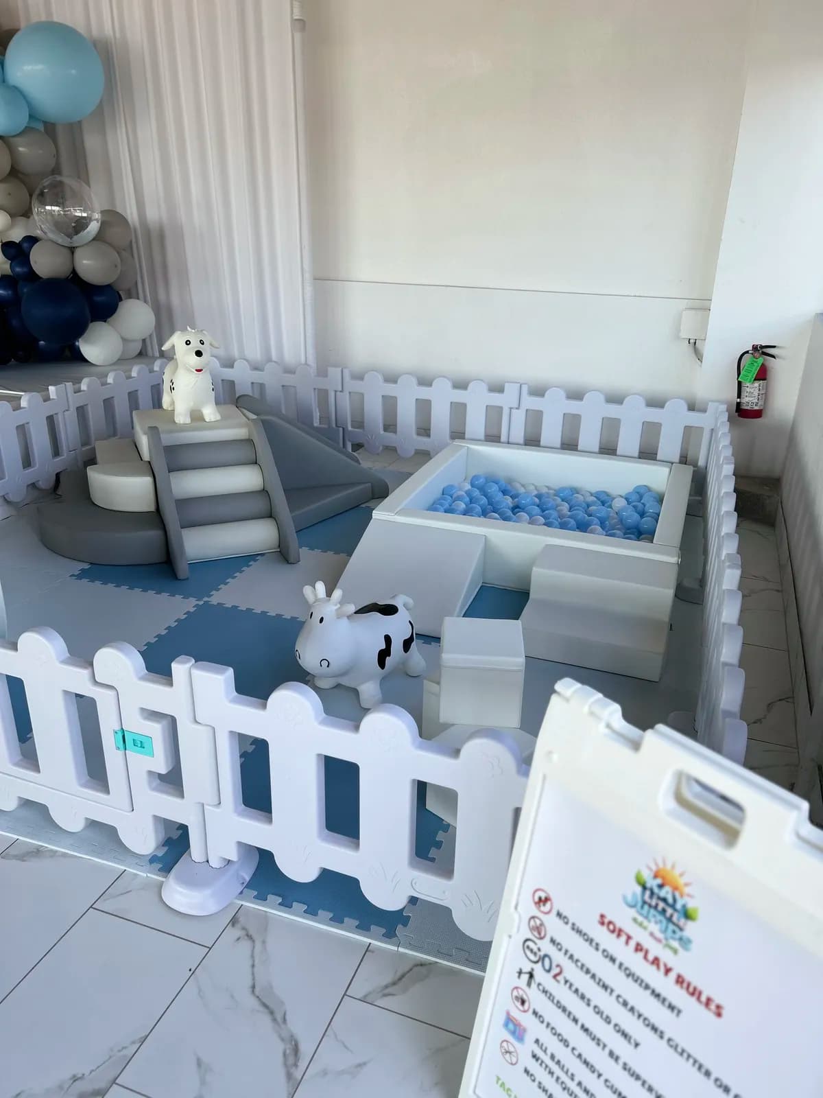 Blue-themed soft play with ball pit, climber, and cow rocker set up indoors